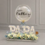 Elegant Father’s Day LED letter arrangement featuring illuminated "PAPA" letters, customized Father’s Day bubble balloon, premium white floral arrangement, and decorative Father's Day accents.