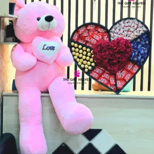 Luxury giant pink teddy bear with premium heart-shaped chocolate and flower gift box featuring KitKat, Ferrero Rocher, Dairy Milk chocolates, and fresh red roses for romantic surprises in Bangladesh.