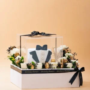 Luxury Father's Day cake arrangement featuring a tuxedo-themed cake inside a transparent acrylic box, surrounded by premium white and ferrero rocher with elegant black ribbon decoration.